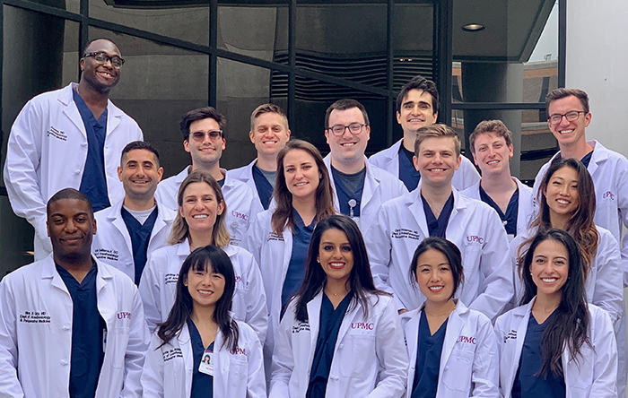 "Clinical Base Year program class pose for a group photo in blue scrubs and white lab coats"